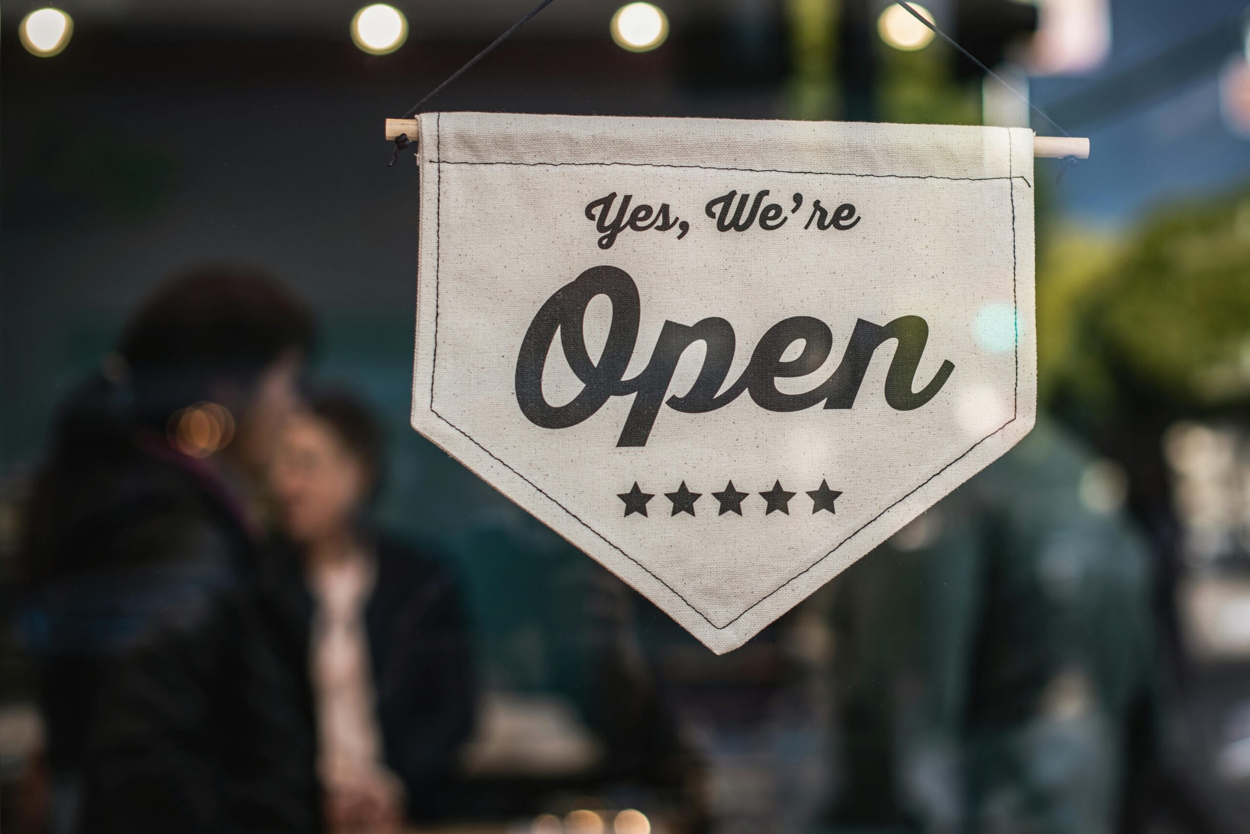 Welcoming open sign displayed in a shop window with blurred background.